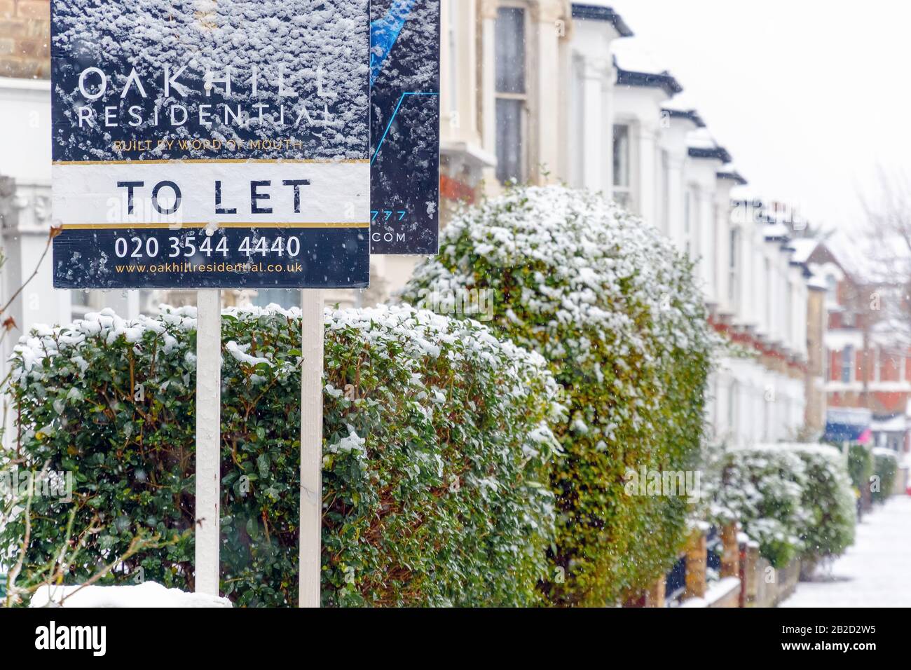 London, UK - December 10, 2019 - To Let sign covered by winter snow around West Hampstead area with terrace houses in the background Stock Photo