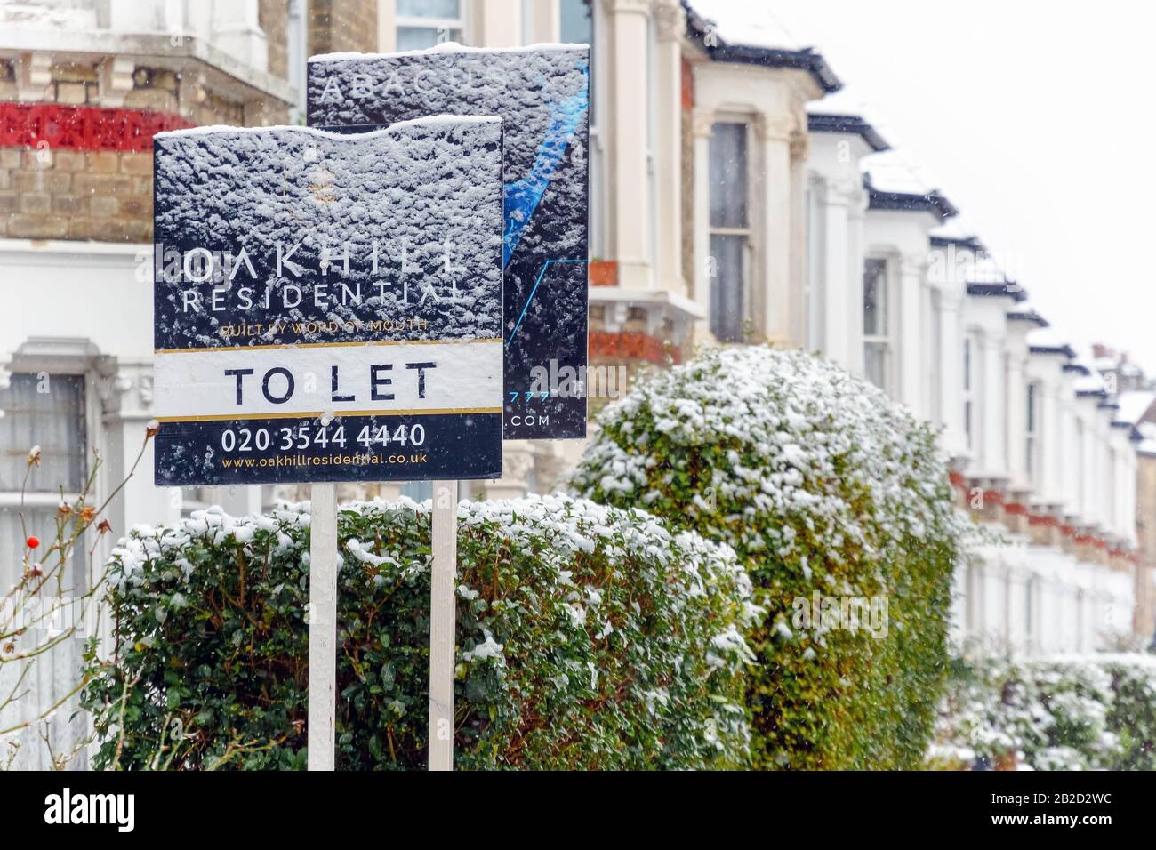 London, UK - December 10, 2019 - To Let sign covered by winter snow around West Hampstead area with terrace houses in the background Stock Photo