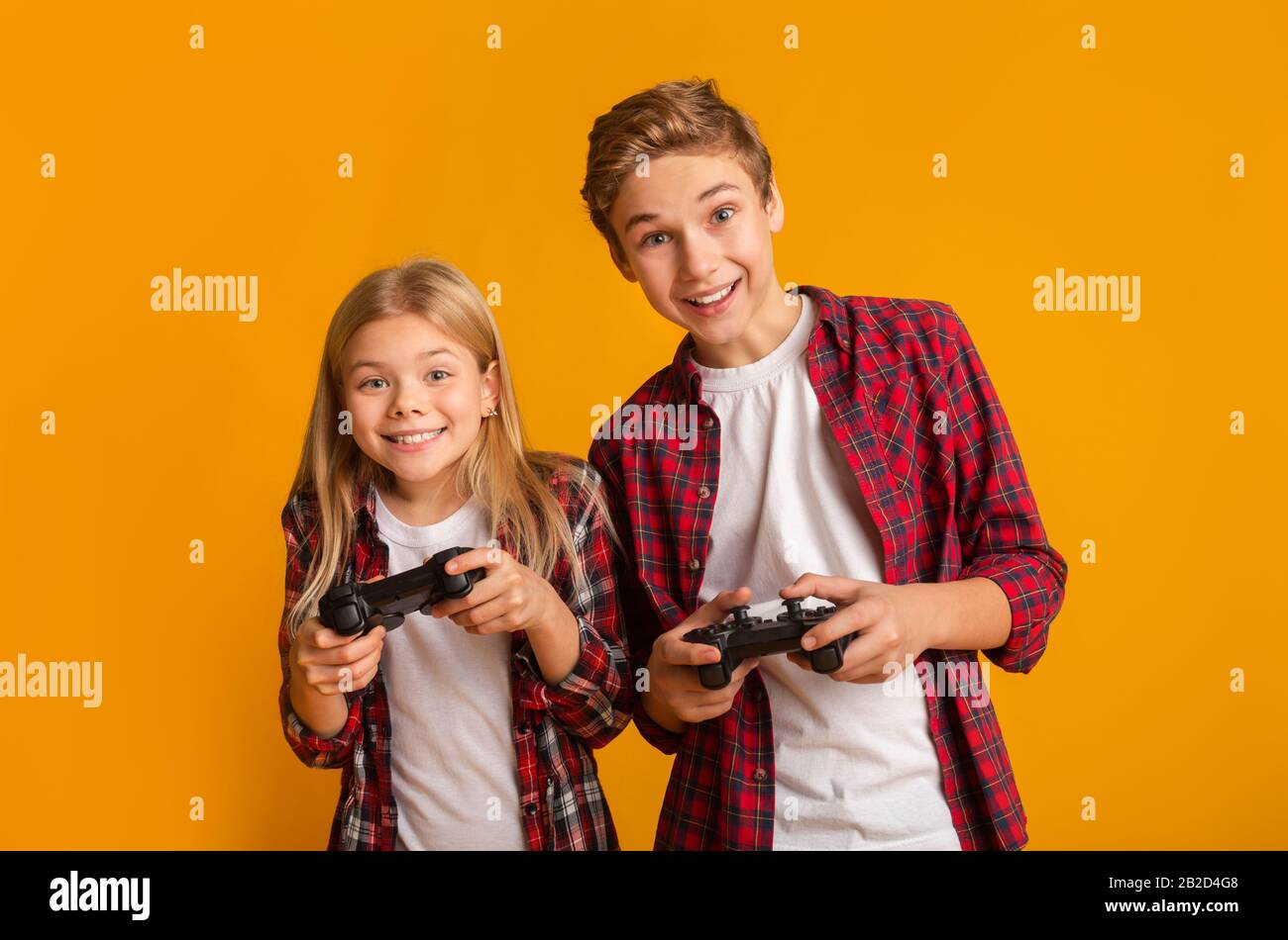Kids Leisure. Brother And Sister With Joysticks Posing Over Yellow Background Stock Photo