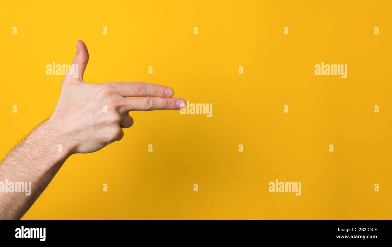 man hand imitating gun over a wide yellow background with copyspace Stock Photo