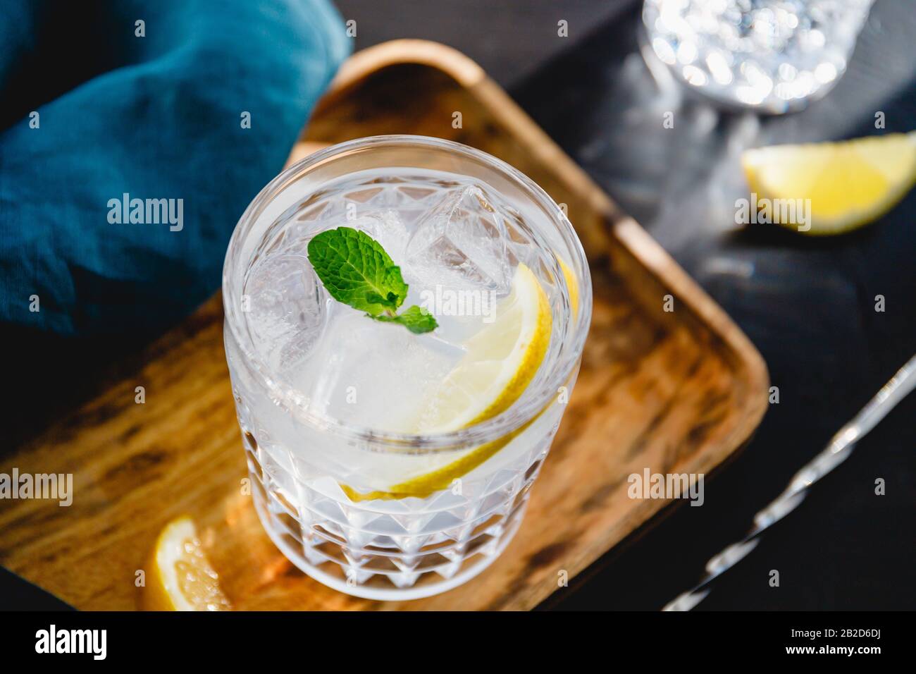 Refreshing cold summer cocktail with soda water, lemon and ice cubes on a wooden tray. Stock Photo