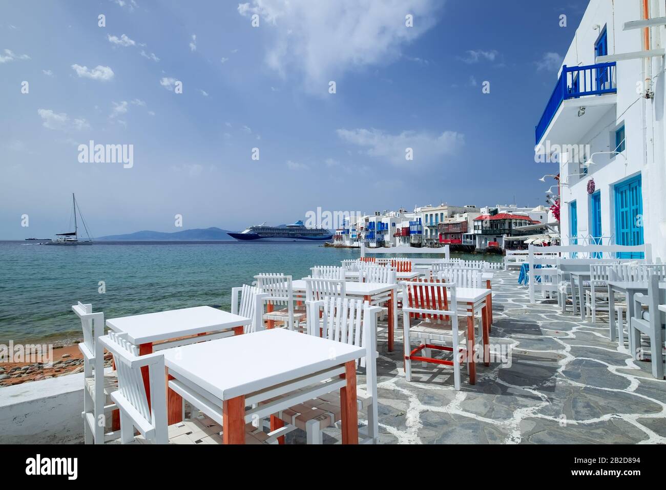 Outdoor restaurant with sea view near romantic colorful Little Venice at sunny day. Yachts on Aegean sea. Amazing touristic place, People walking alon Stock Photo
