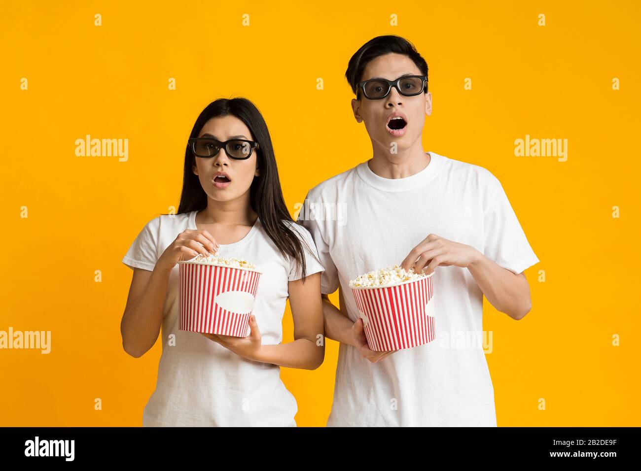 Stunned asian couple in 3d glasses watching movie with popcorn Stock Photo