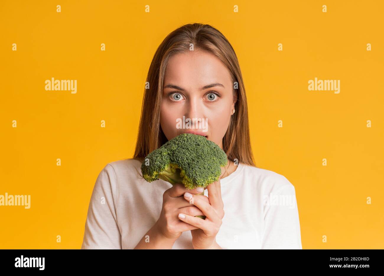 Young Woman Eating Broccoli, Biting Healthy Vegetable With Wide-Opened Eyes Stock Photo