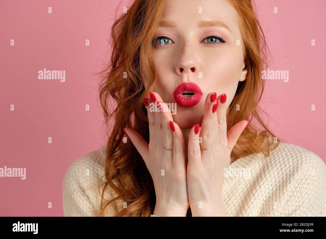 A Red Haired Curly Haired Girl With Red Lips Blows A Kiss While Looking At The Camera Standing