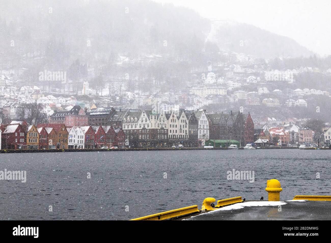 Winter in Bergen, Norway. Snowing heavily. View from the old port of the city, Vaagen. UNESCO Hanseatic architecture at Bryggen. Mount Floeyen (Fløyen Stock Photo