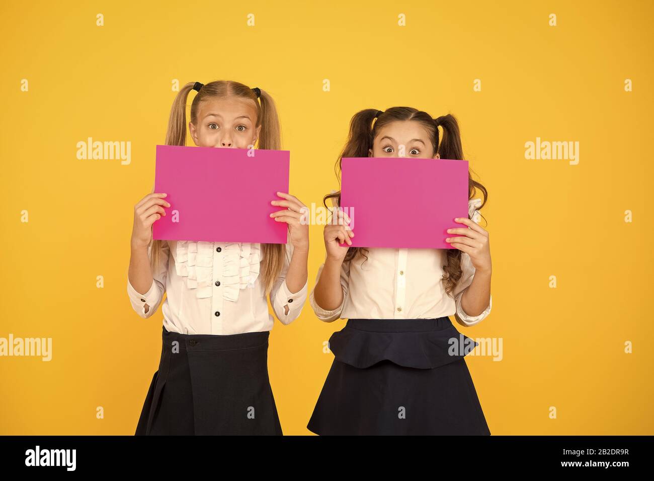 Drawing attention. Happy kids holding empty sheets of paper. Little kids smiling with pink drawing papers. Small kids smiling with blank advertisement posters. Cute kids advertising, copy space. Stock Photo