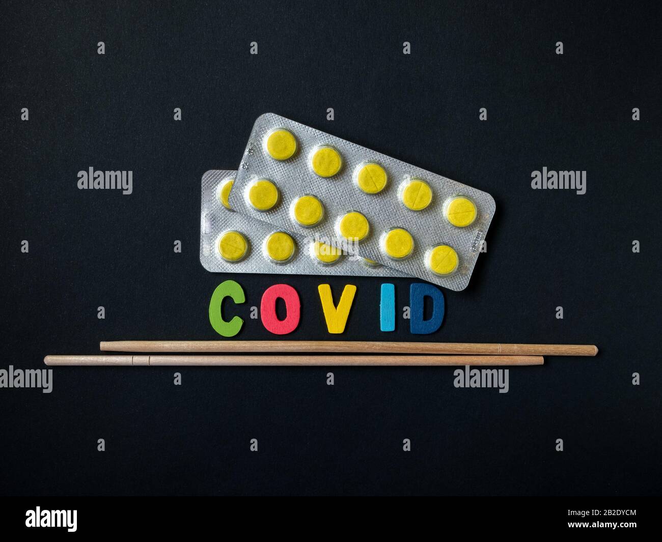 Blisters with yellow pills, the inscription denoting a virus and Asian chopsticks on a black background.  Symbol of treats from Asia in the form of co Stock Photo