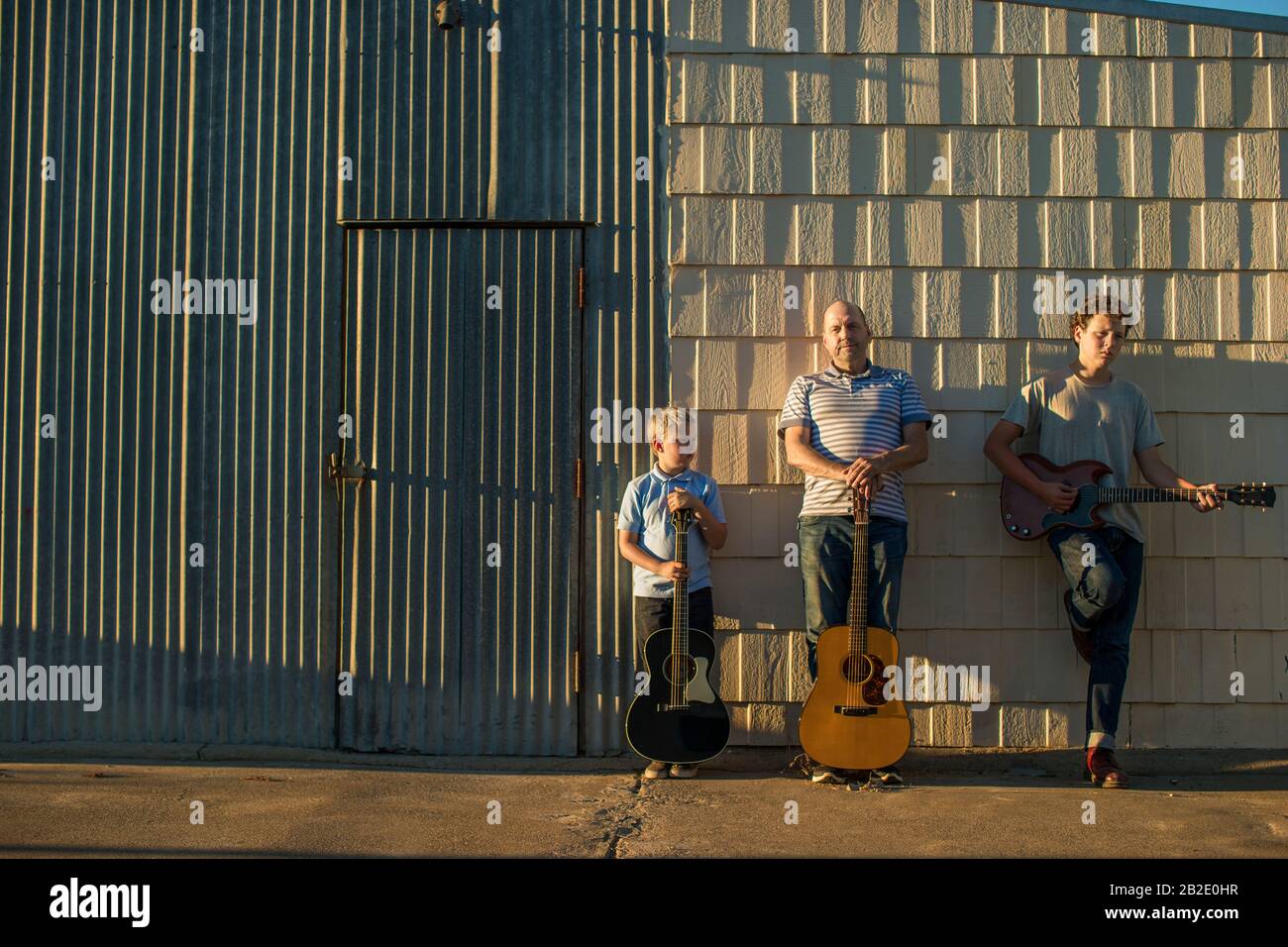 Middle aged father with this two sons standing with their guitars outside a building Stock Photo