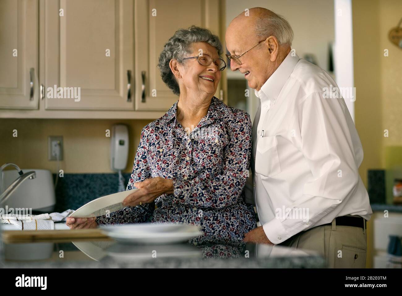 Happy elderly couple share an affectionate moment while washing dishes together Stock Photo