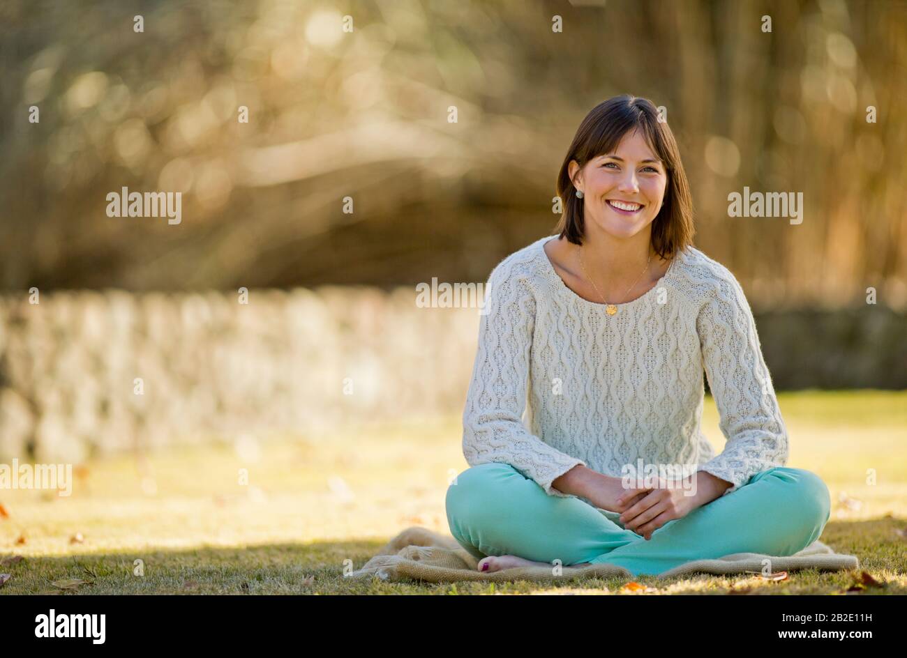 Portrait of a smiling young woman relaxing on a blanket in a sunlit park Stock Photo