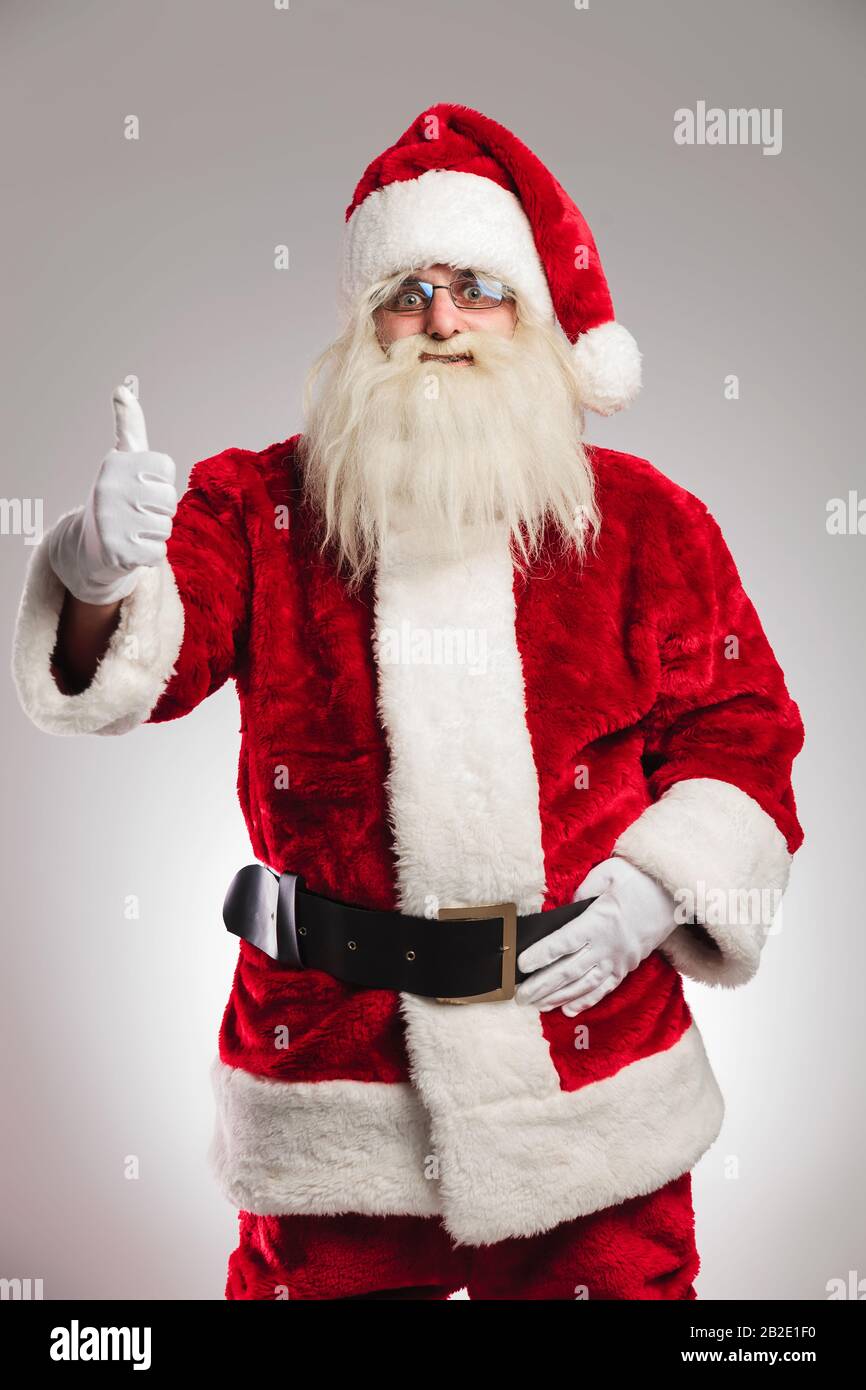 portrait of a positive santa claus making the thumbs up gesture on grey ...