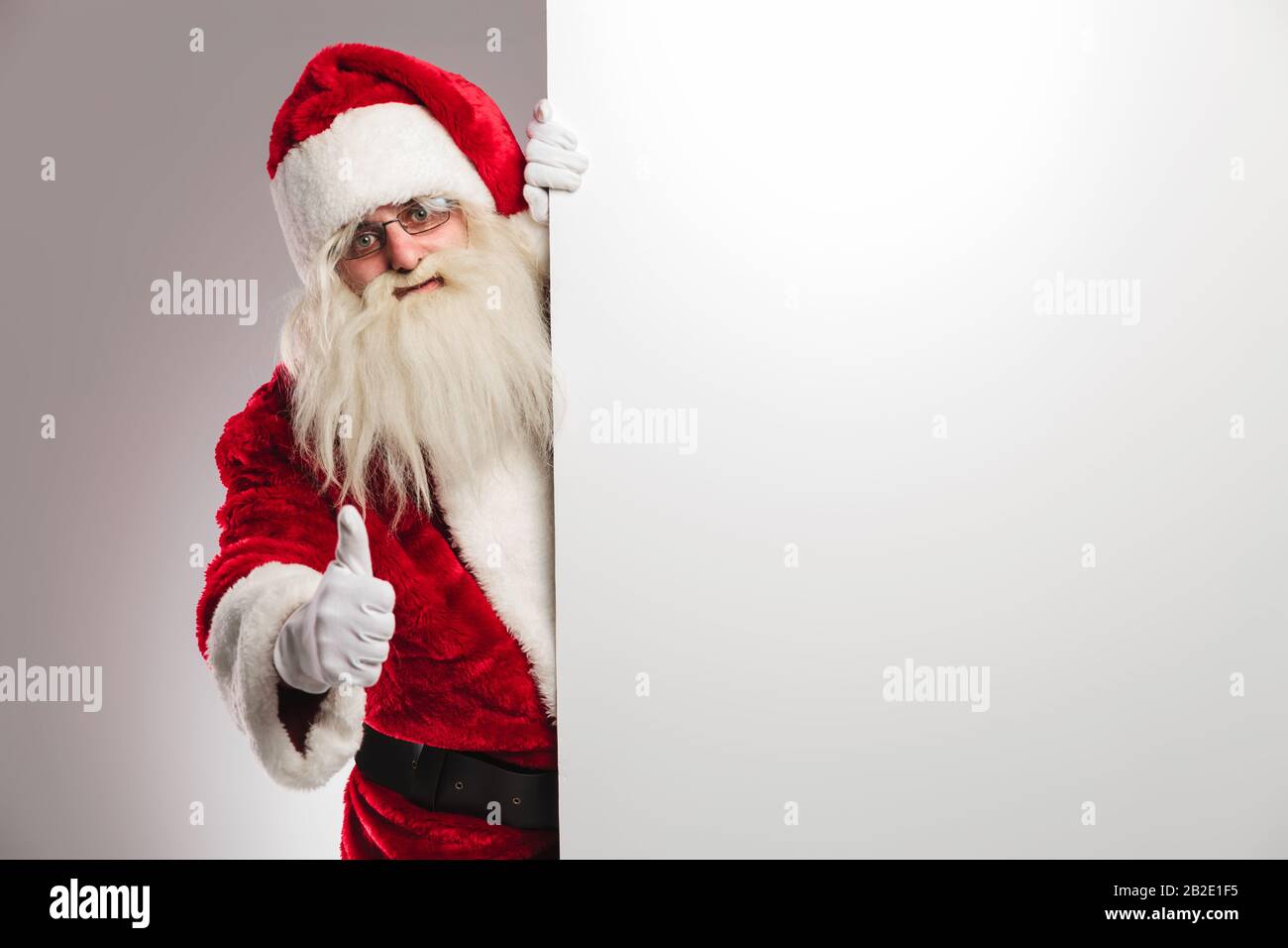 santa claus making ok sign while presenting blank board on grey ...