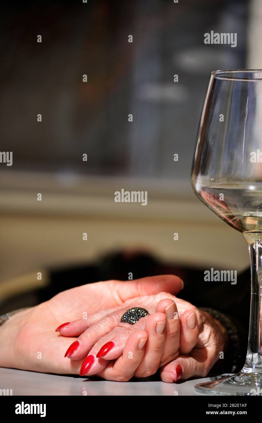Elderly mother holding daughter's hand on a restaurant table with a glass of white wine next to them. Day time sharing with the mother. Hands holding Stock Photo