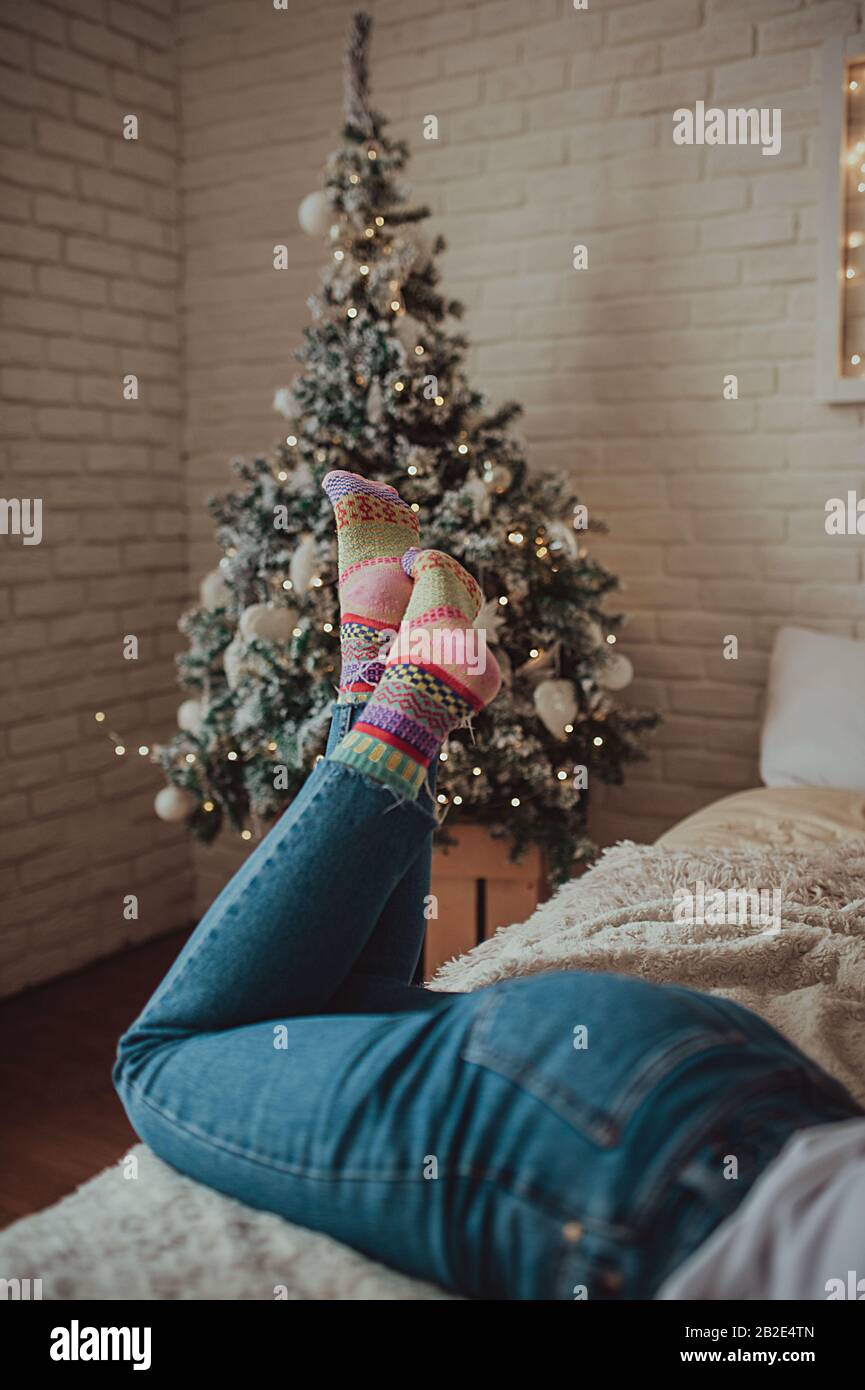 upright female legs in skinny jeans and bright knitted socks on a bright  bed against the background of the Christmas tree Stock Photo - Alamy