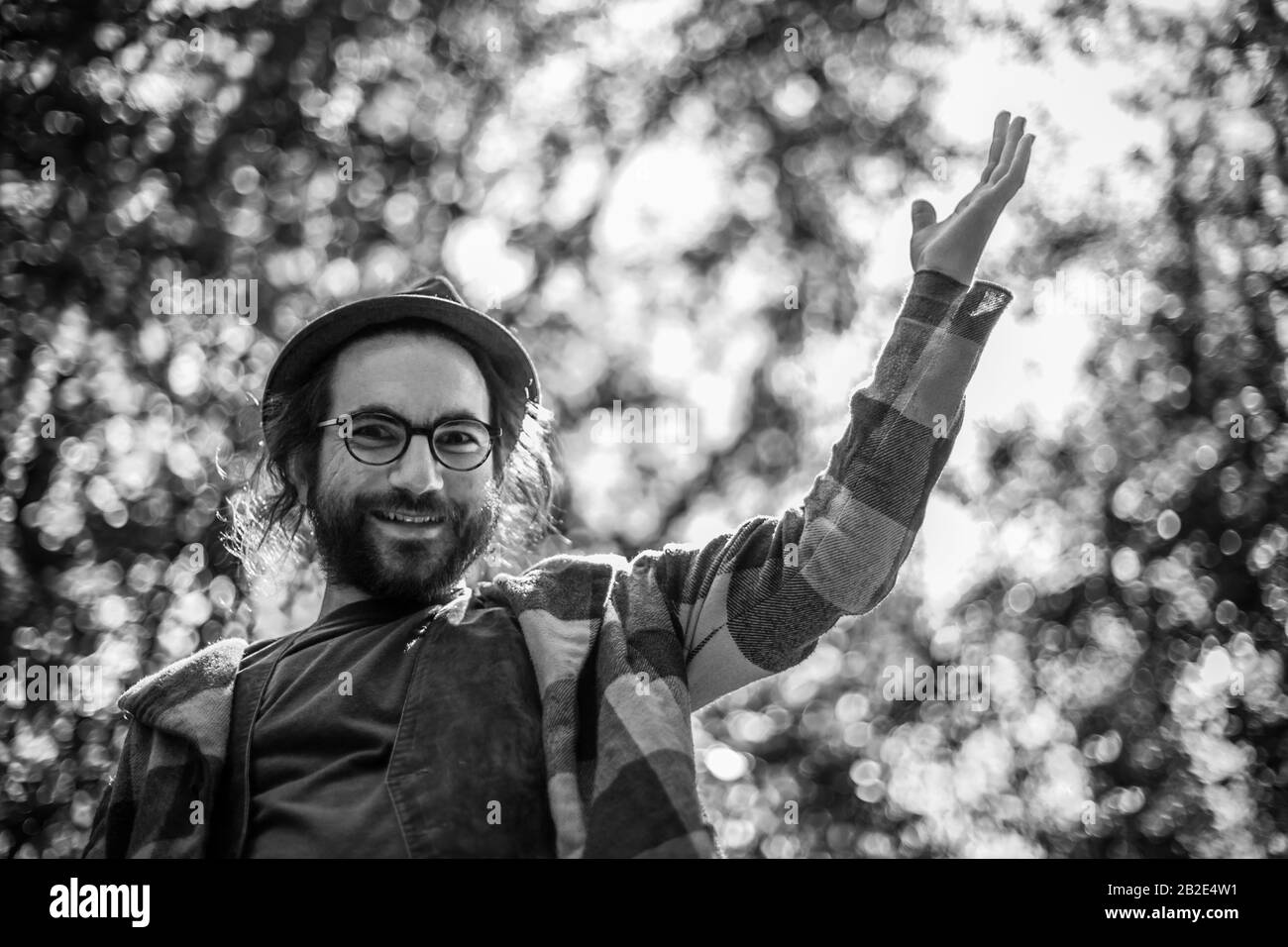 A successfully looking business man celebrating his next achievement. Black and white portrait of a young bearded man with glasses raising his hand up Stock Photo