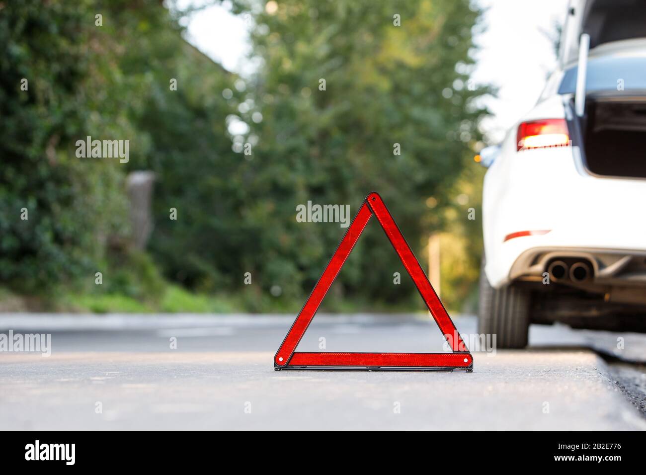 Close up of red warning triangle sign symbol and broken white car on roadside, copy space. Stock Photo