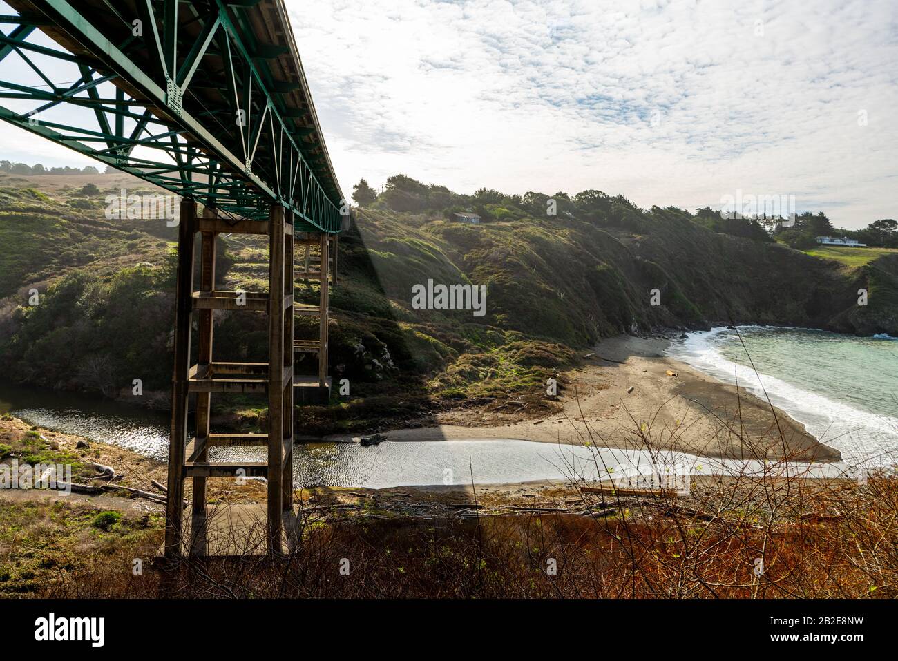 Low view of bridge above river leading to beach by cliffside houses Stock Photo