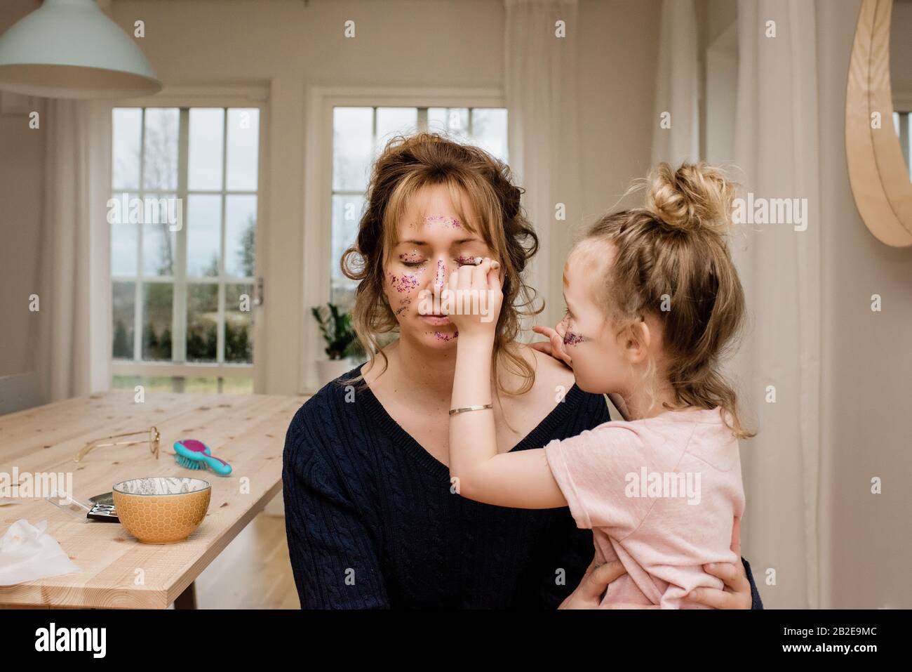 mother and daughter playing dress up with make up & glitter together Stock Photo