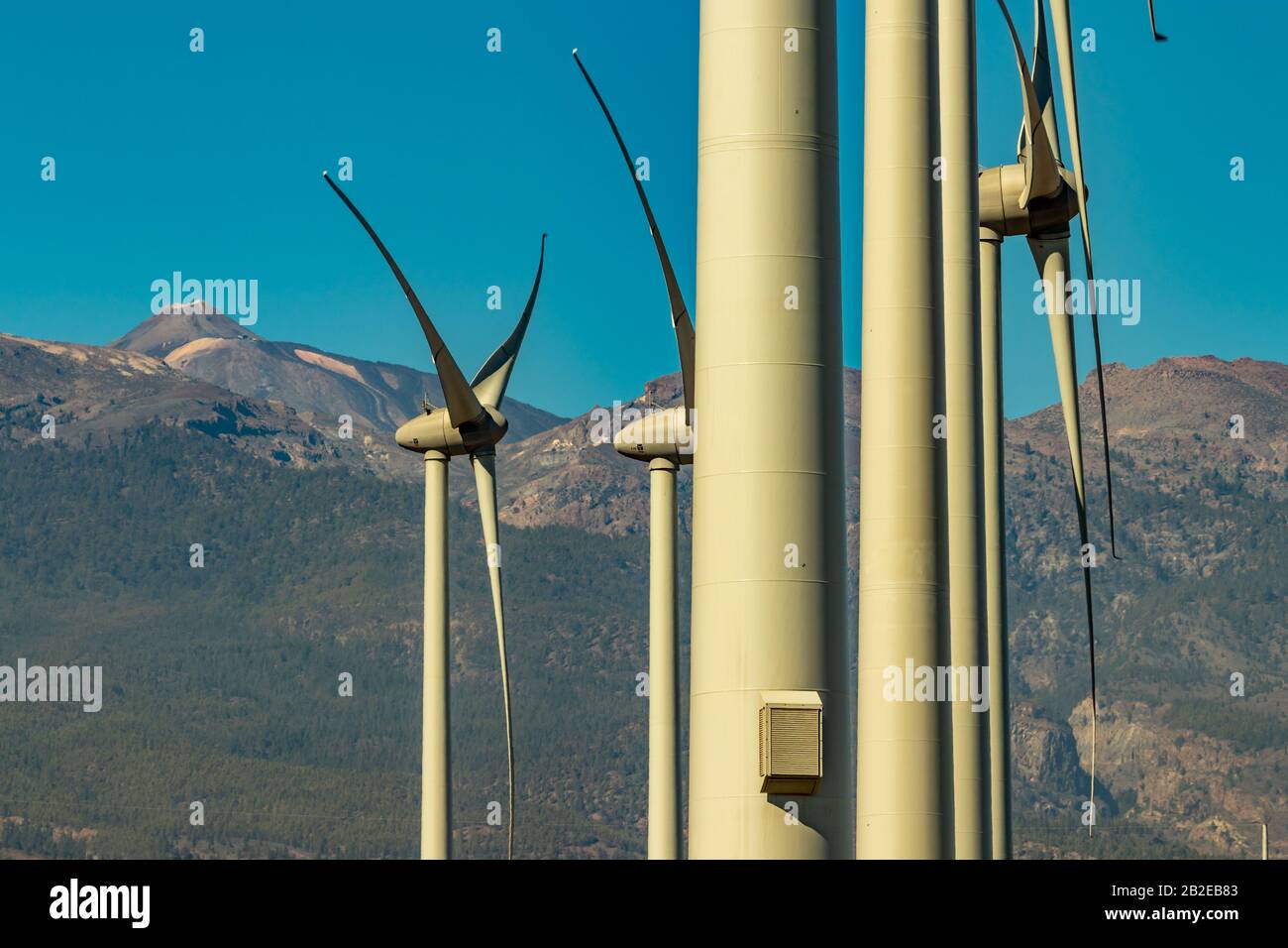 Wind power stations. A row of turbines near the seashore. Wind farm eco field. Eolic park with mount Teide and blue sky in background. Green, ecologic Stock Photo