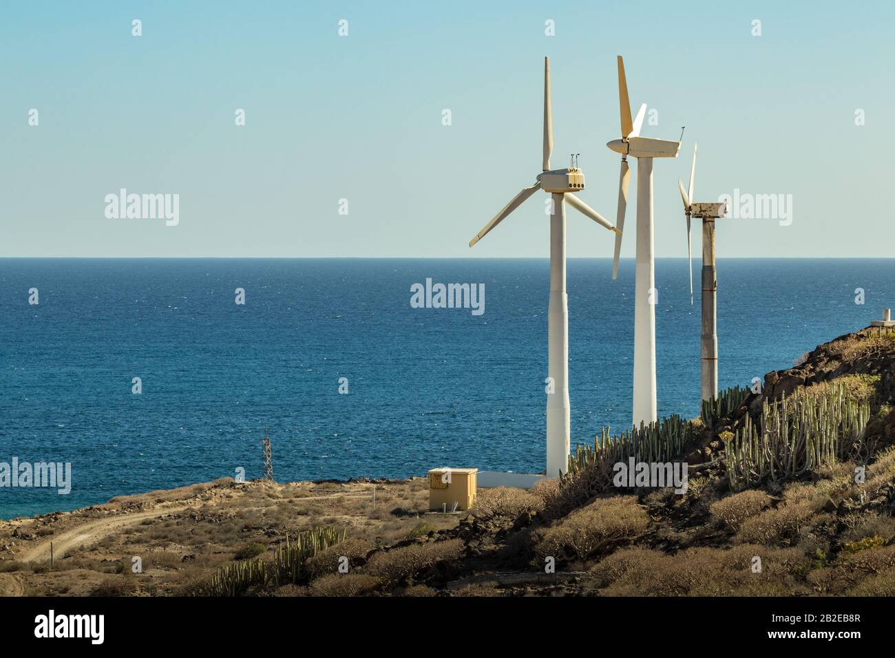 Wind power stations. A row of turbines near the seashore. Wind farm eco field. Eolic park with blue sky in background. Green, ecological and power ene Stock Photo