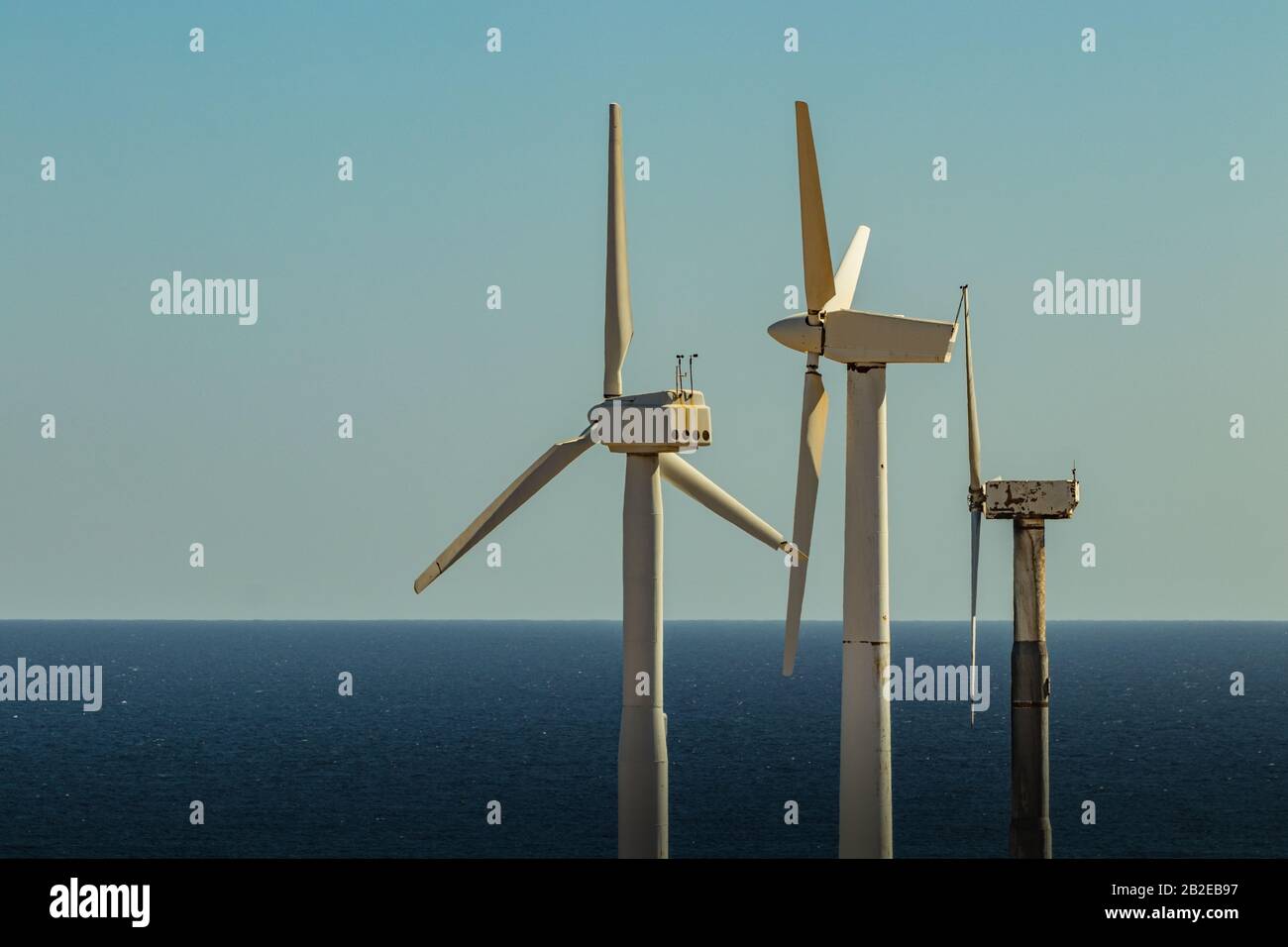 Wind power stations. A row of turbines near the seashore. Wind farm eco field. Eolic park with blue sky in background. Green, ecological and power ene Stock Photo
