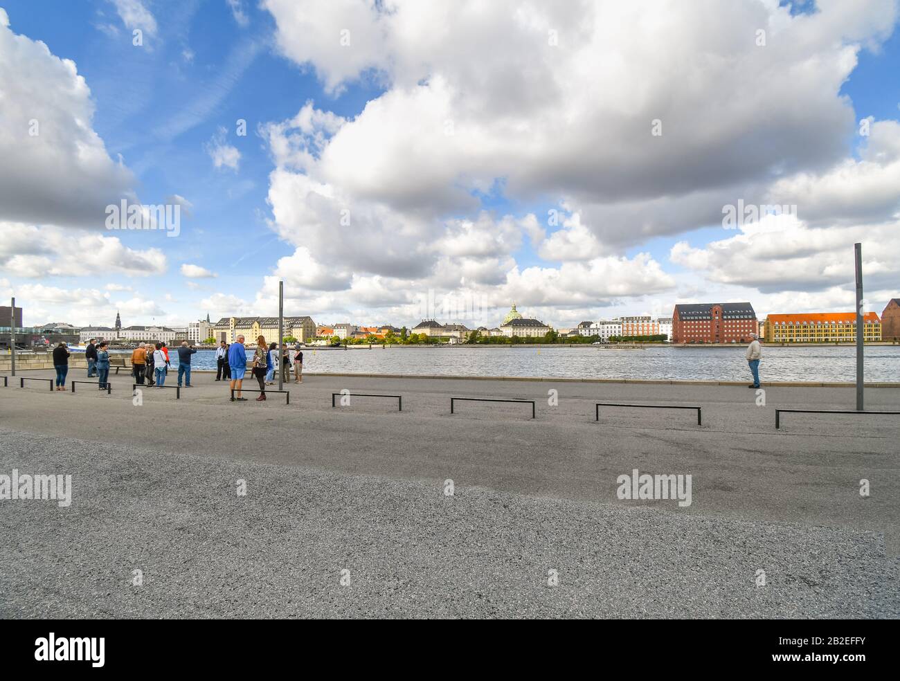 A group of tourists stand near the Opera House and along the waterfront on the island of Holmen and look across at the skyline of Copenhagen Denmark. Stock Photo