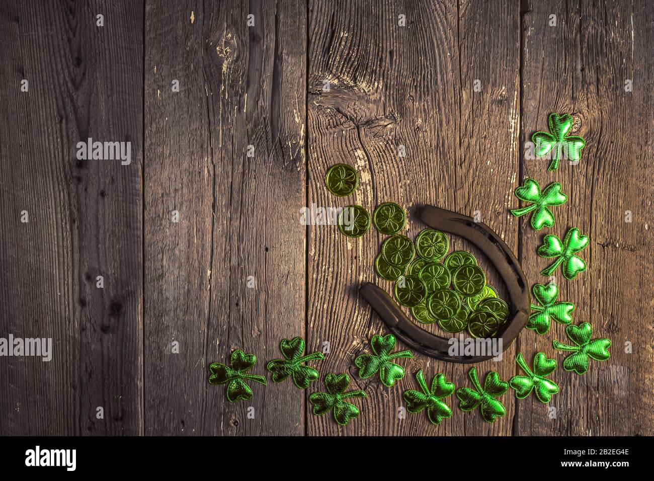 Background with rusty horseshoe and clover leaves and coins over rustic wood. St.Patrick's day holiday symbol. Lucky charms. Top view, copy space. Stock Photo