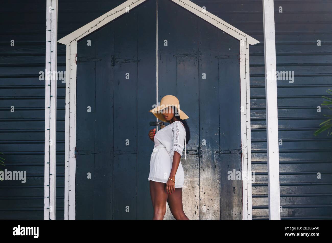 Black woman aged 25 to 30, in front of a church door, dressed in white modeling, fresh summer and tropical clothes. Stock Photo