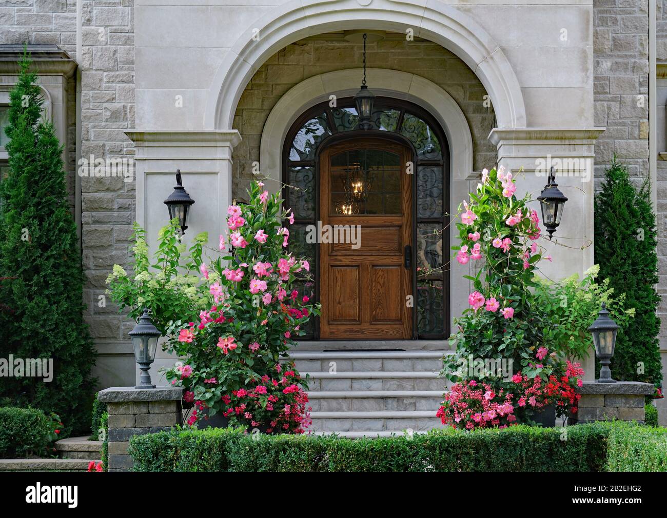 front door of elegant stone fronted house with large standing amaryllis flowers Stock Photo