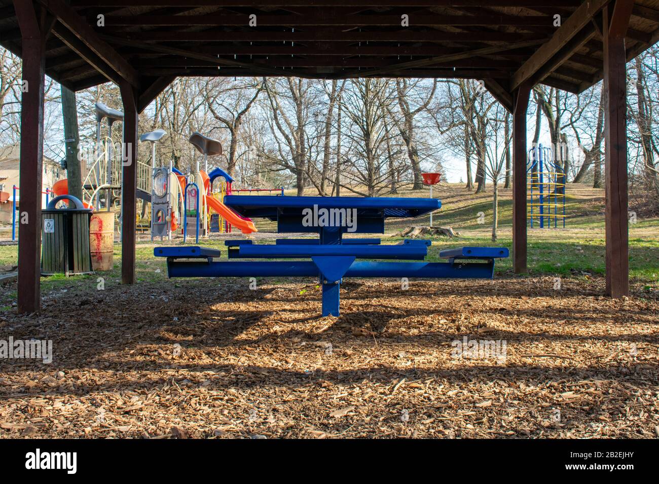 A Wooden Gazebo in a Park With Blue Benches Under it and a Playground ...