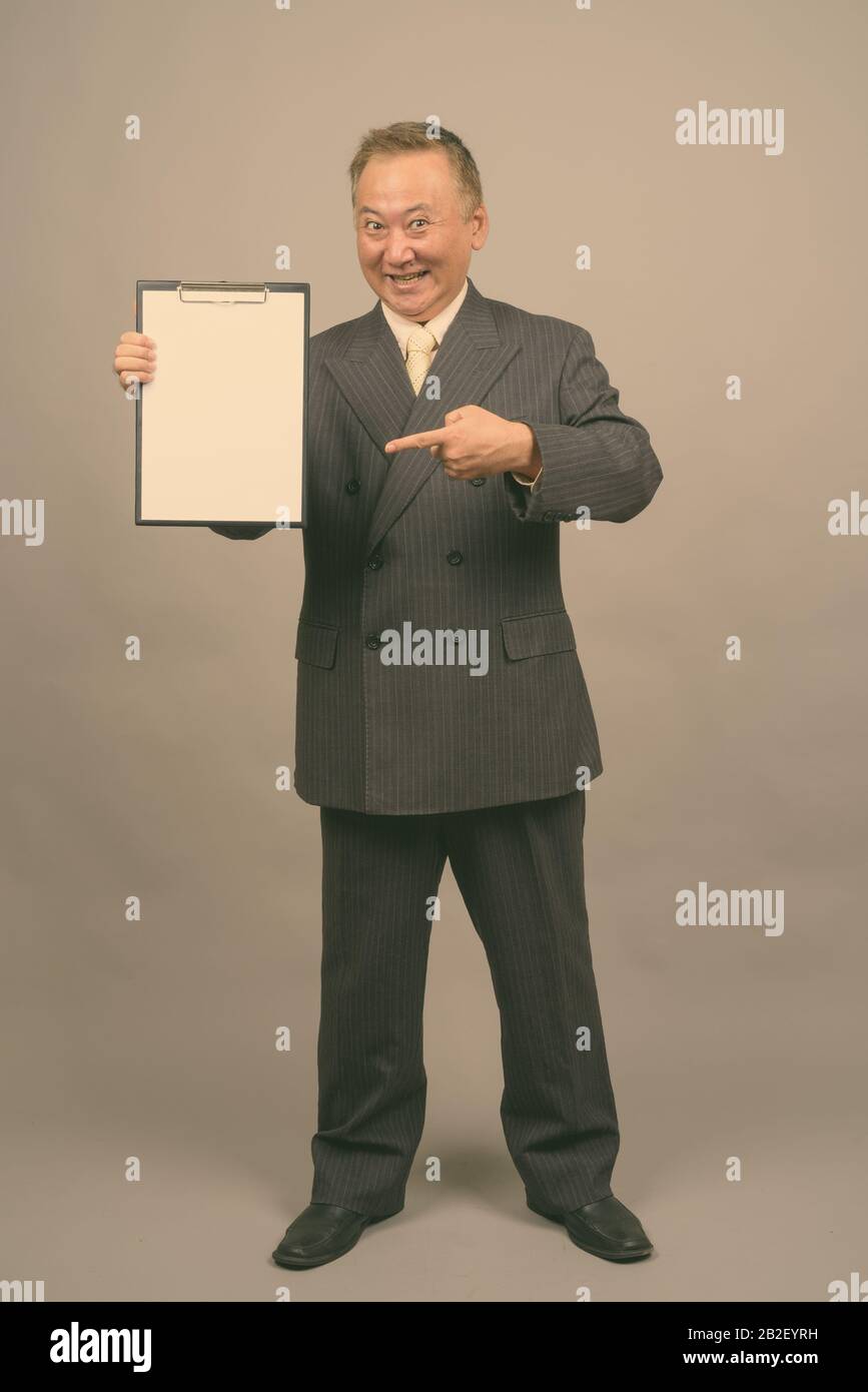 Studio shot of mature Asian businessman holding clipboard against gray ...