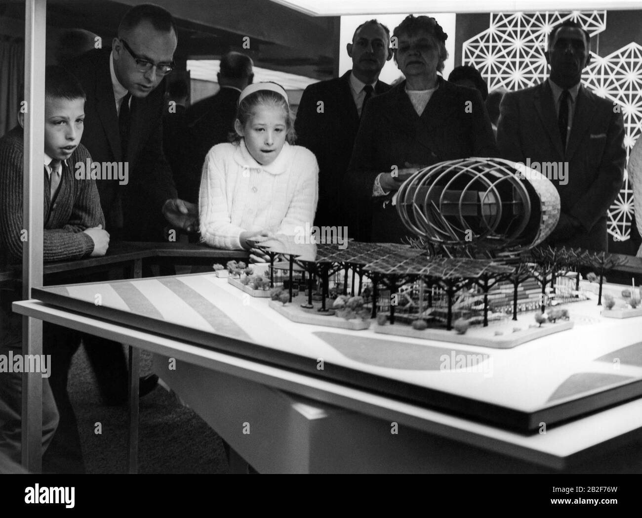 Children and adults viewing an architectural design model of the IBM pavilion with man-made steel trees and Ovoid Theater, designed by Charles Eames and Eero Saarinen for the 1964 New York World's Fair. The pavilion model was on display at the IBM Business Show in Manhattan at the New York Coliseum, circa April 30,1963. Stock Photo