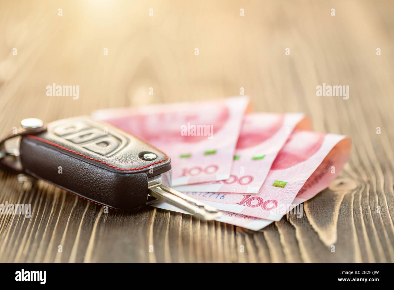 Close up new car keys with Chinese banknote on wooden table. Car purchase or car rental concept Stock Photo