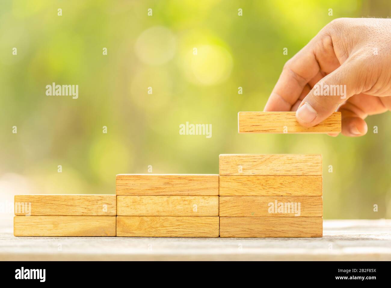 Close up hand holding blocks wood to make step grow up on green blur background with copy space for text or design concept for business concept Stock Photo