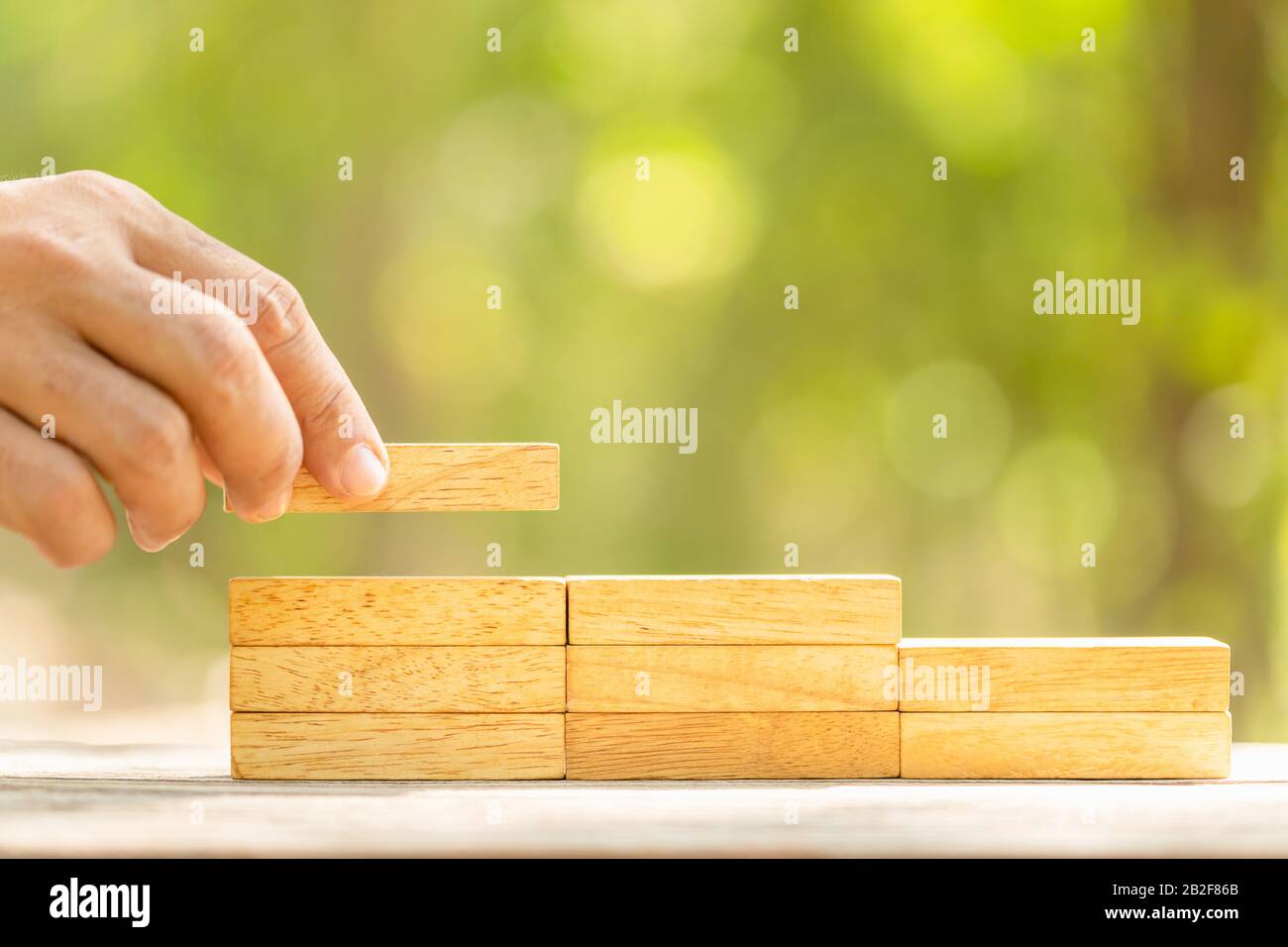 Close up hand holding blocks wood to make step grow up on green blur background with copy space for text or design concept for business concept Stock Photo