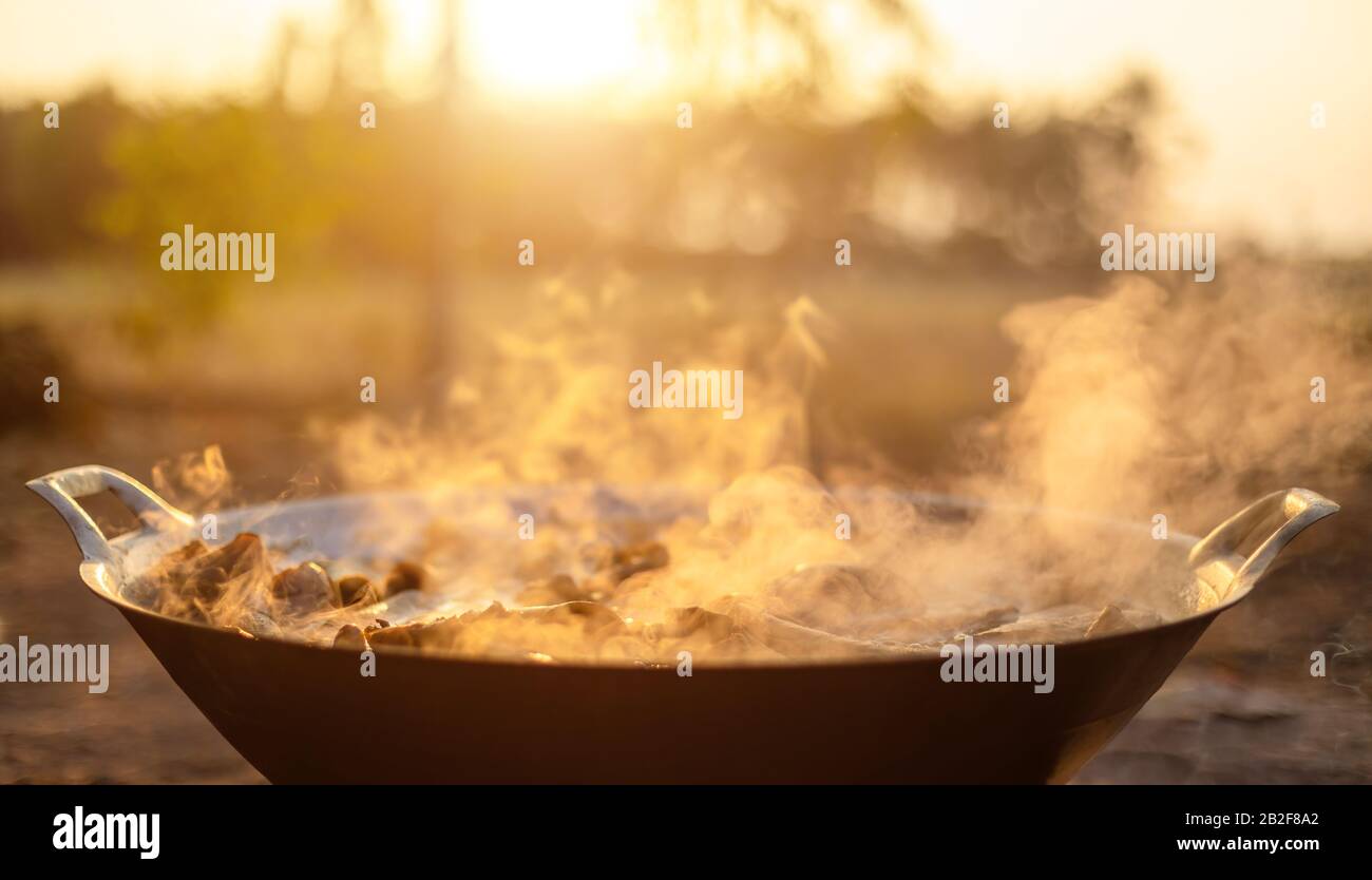 Traditional silver cooking pan with white smoke while cooking on sunset background Stock Photo