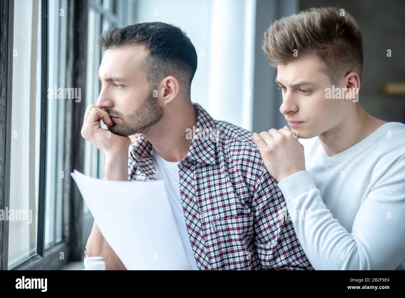 Two young men standing near the window looking desperate Stock Photo