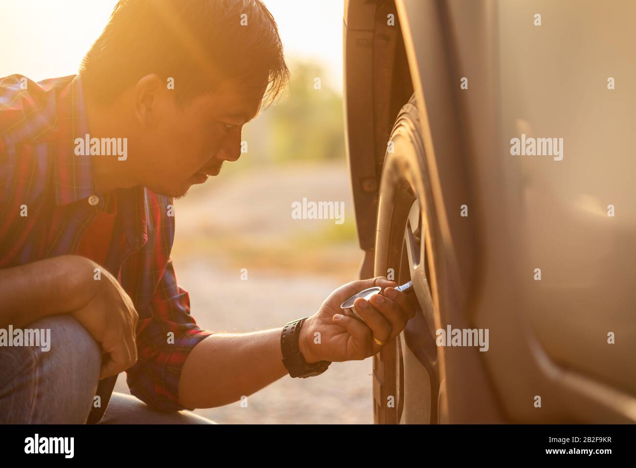 Asian man checking air pressure and filling air in the tires of his car ...