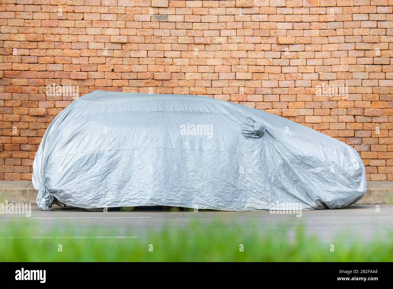 Car covering by silver fabric parking on the road. Car protection concept Stock Photo