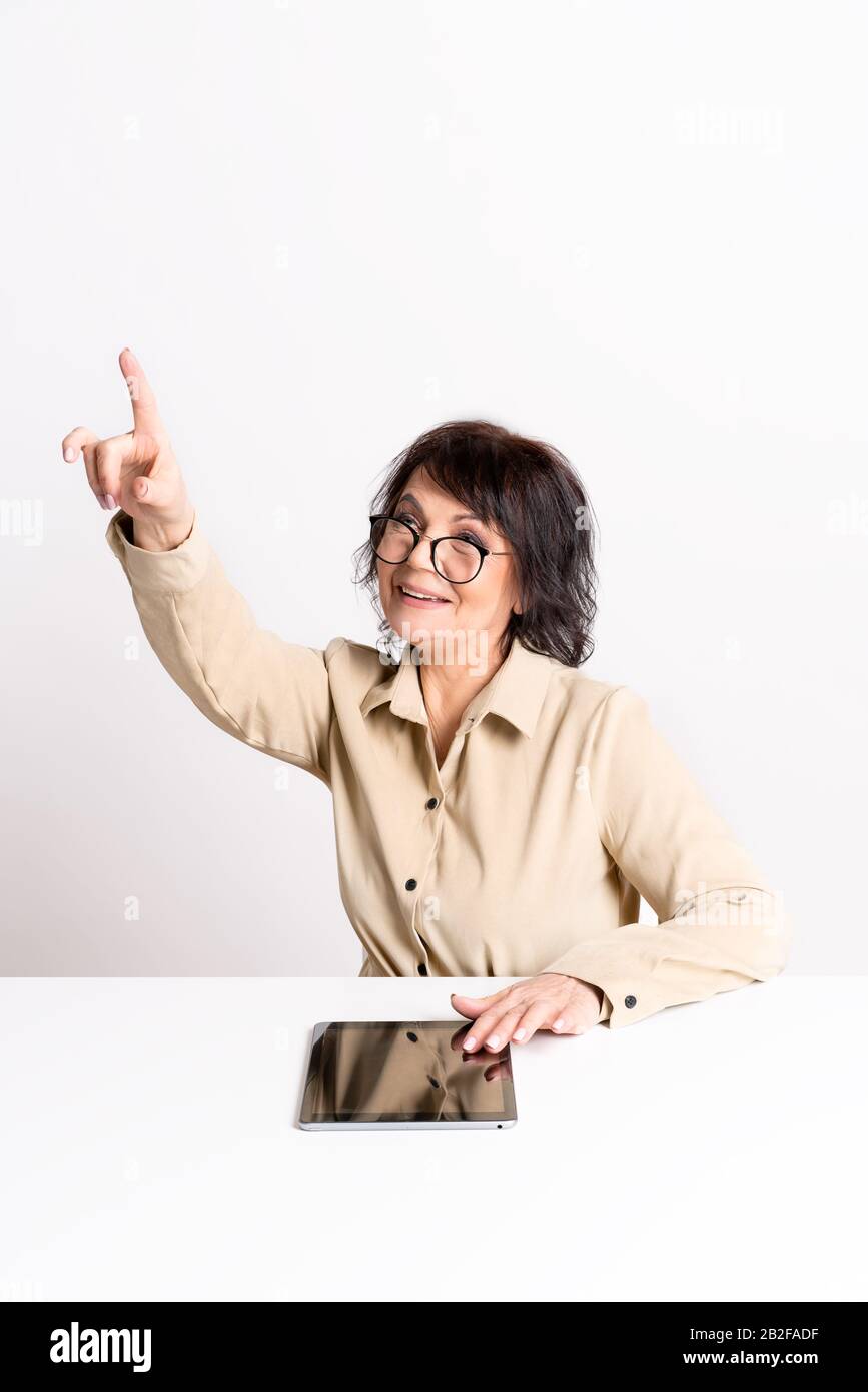 Beautiful Senior woman work at home in glasses and comfortable clothes by smartphone and tablet. Stock Photo