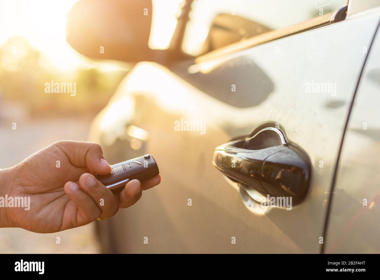 Open the car concept : Hand holding remote car keys and press the button open or lock the silver car at outdoor parking lot with sunlight effect in mo Stock Photo