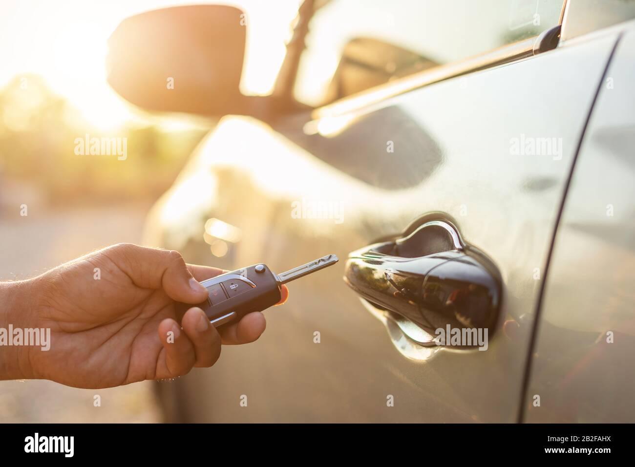 Open the car concept : Hand holding remote car keys and press the button open or lock the silver car at outdoor parking lot with sunlight effect in mo Stock Photo