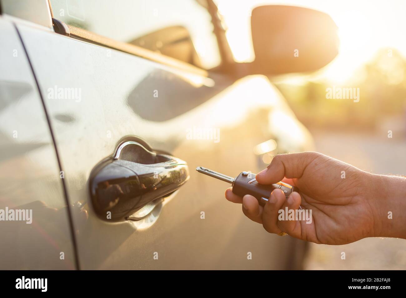 Open the car concept : Hand holding remote car keys and press the button open or lock the silver car at outdoor parking lot with sunlight effect in mo Stock Photo