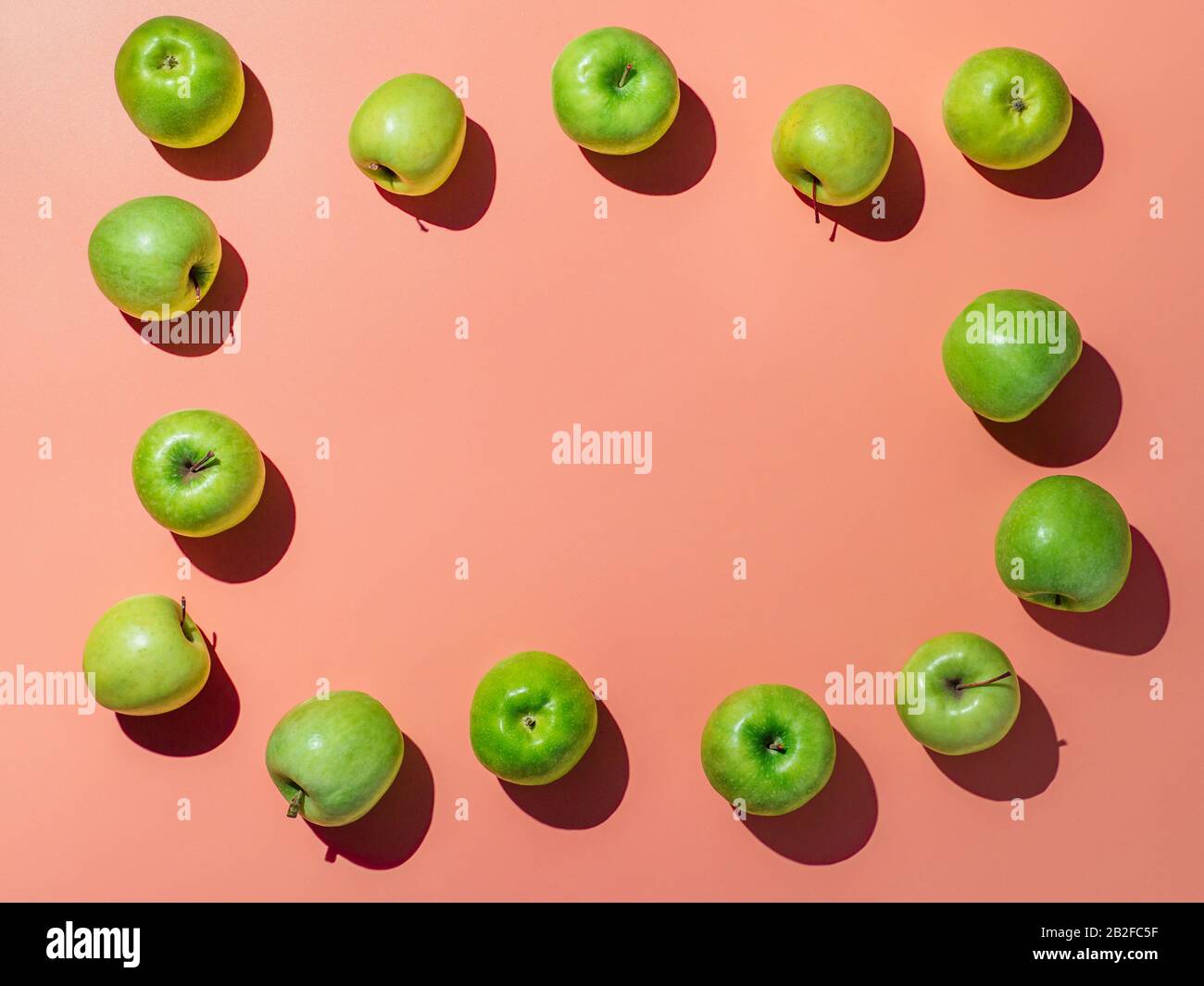 Green apples on orange or coral pink background with copy space for text or design in center, Colorful fruit frame. Flat lay or top view, Hard light Stock Photo