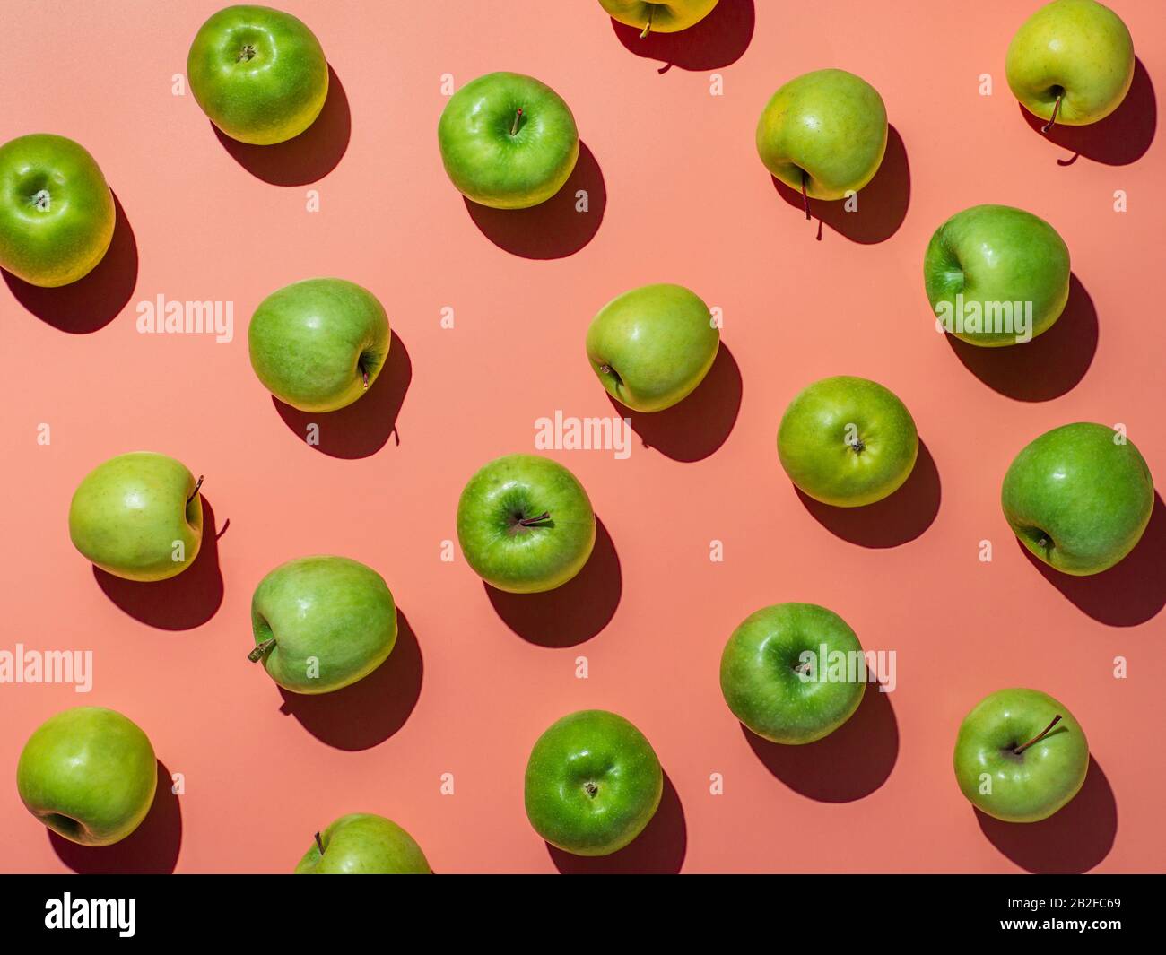 Green apples on orange or coral pink background pattern. Colorful fruit frame. Flat lay or top view, Hard light. Creative concept. Stock Photo