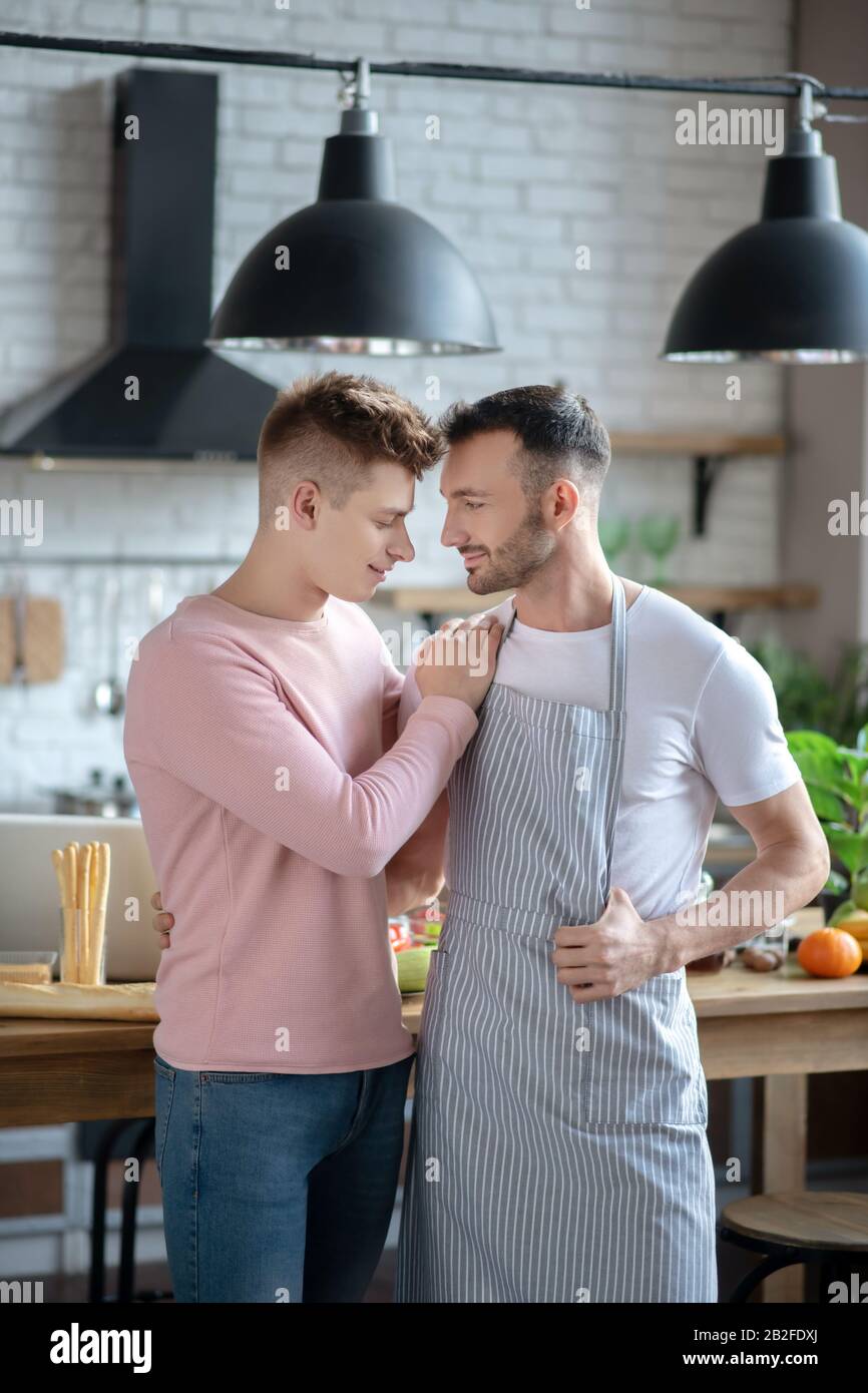 Two young men standing hugging in the kitchen. Stock Photo