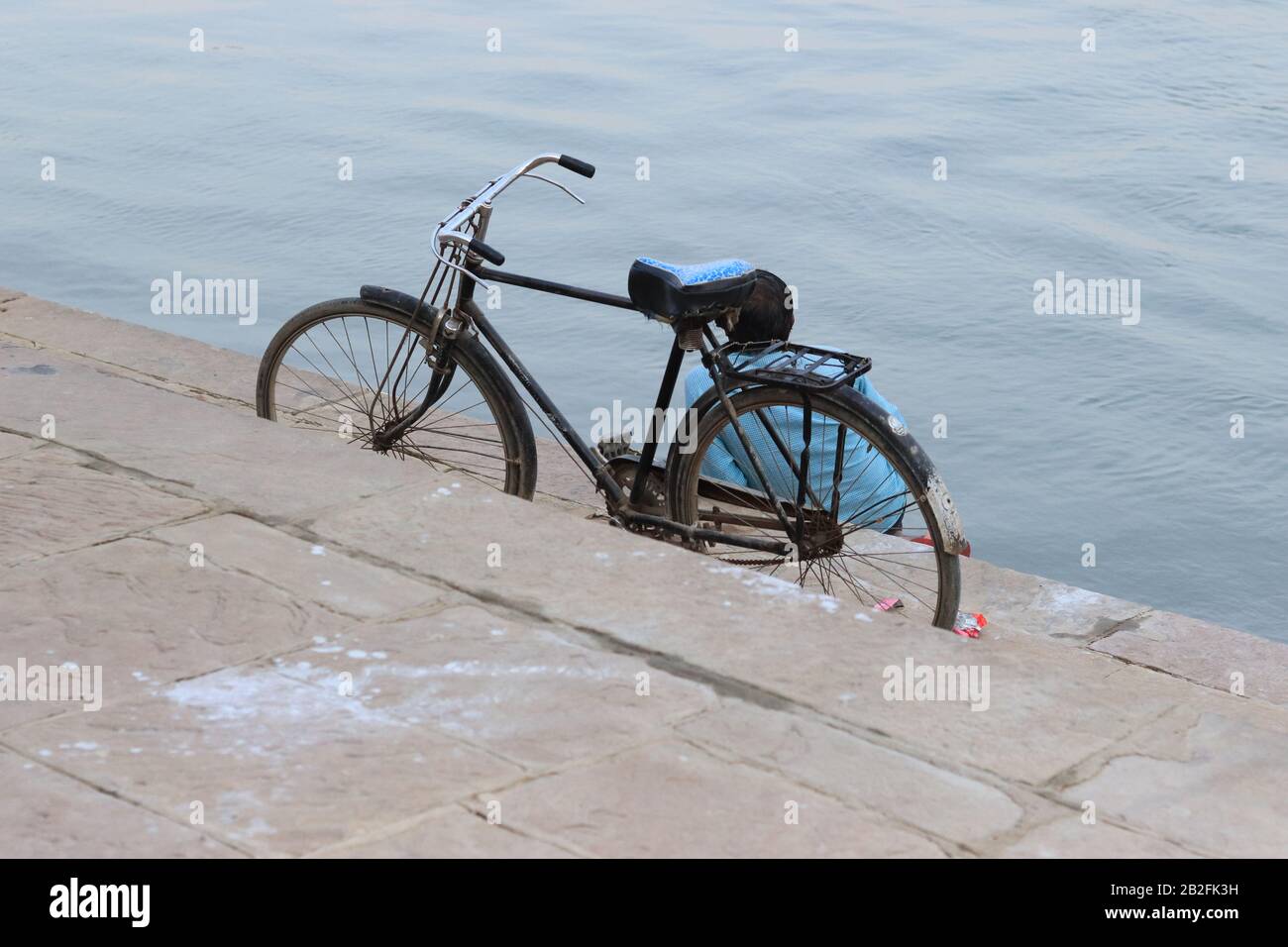 A man with bicycle sitting on the ghat of Ganga River Stock Photo