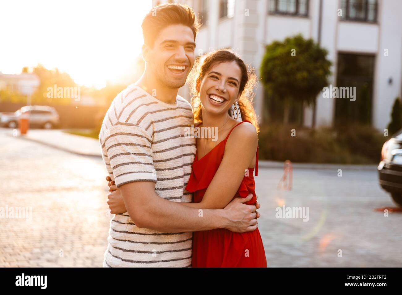 Image of joyful caucasian couple in summer clothes laughing and hugging while walking on city street Stock Photo