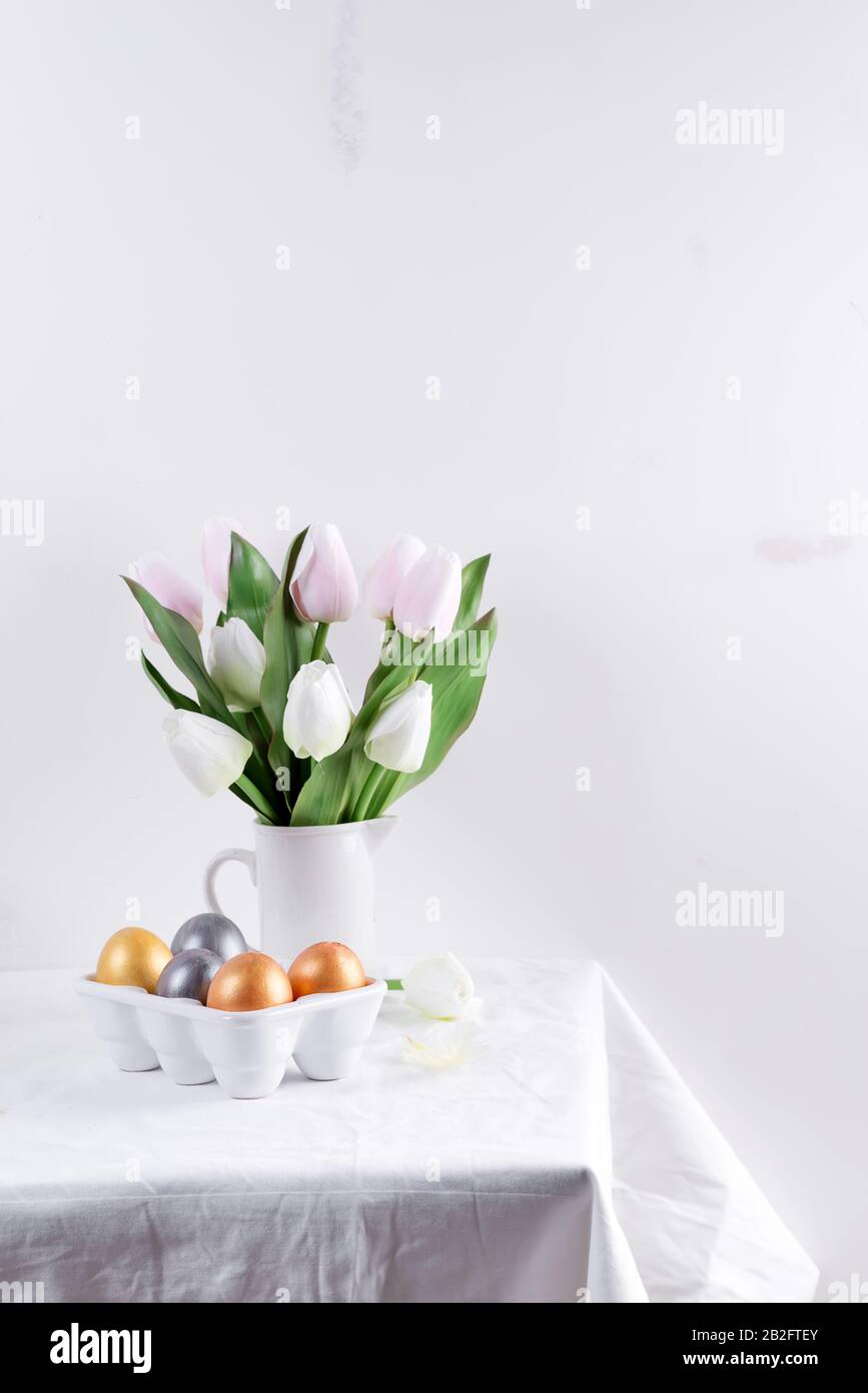 Golden Easter Eggs in ceramic egg tray with tulip on white table. Easter background or easter concept. Stock Photo